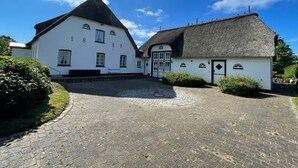 A traditional building with a thatched roof, white walls, and a cobblestone driveway.