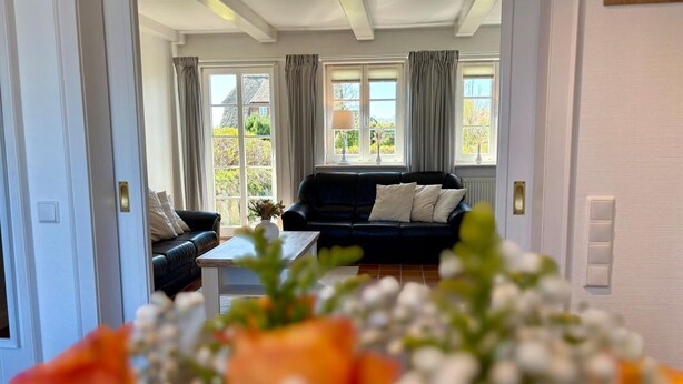 Ein Wohnzimmer mit einer schwarzen Couch, einem weißen Couchtisch und Blick ins Freie durch große Fenster.