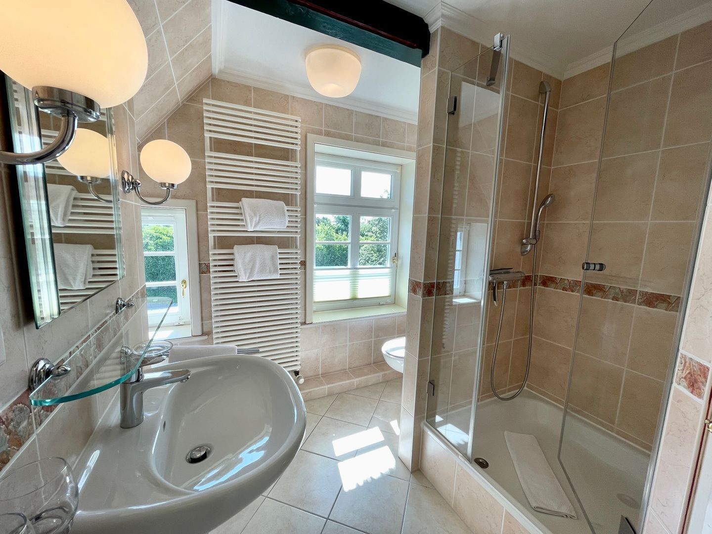 A modern bathroom with a glass-enclosed shower, a large sink, and a window providing natural light.