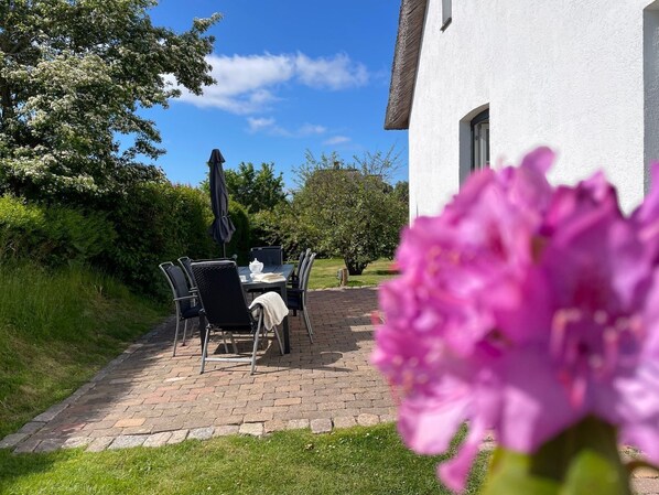 A patio with a table and chairs, a thatched roof, and a white building in the background.