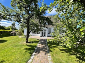 A white building with a stone pathway leading to a door, surrounded by lush greenery and a clear blue sky. - 3 Liv: 55 sqm on three levels offer plenty of space for up to 4 people - country house (Sylt)