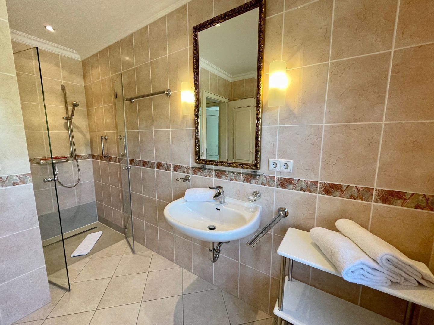 A bathroom with a glass shower enclosure, a sink with a mirror above it, and a towel rack with towels.