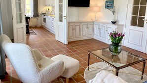 Ein geräumiger Wohnbereich mit einer Couch, einem Glastisch und einer Küche im Hintergrund.