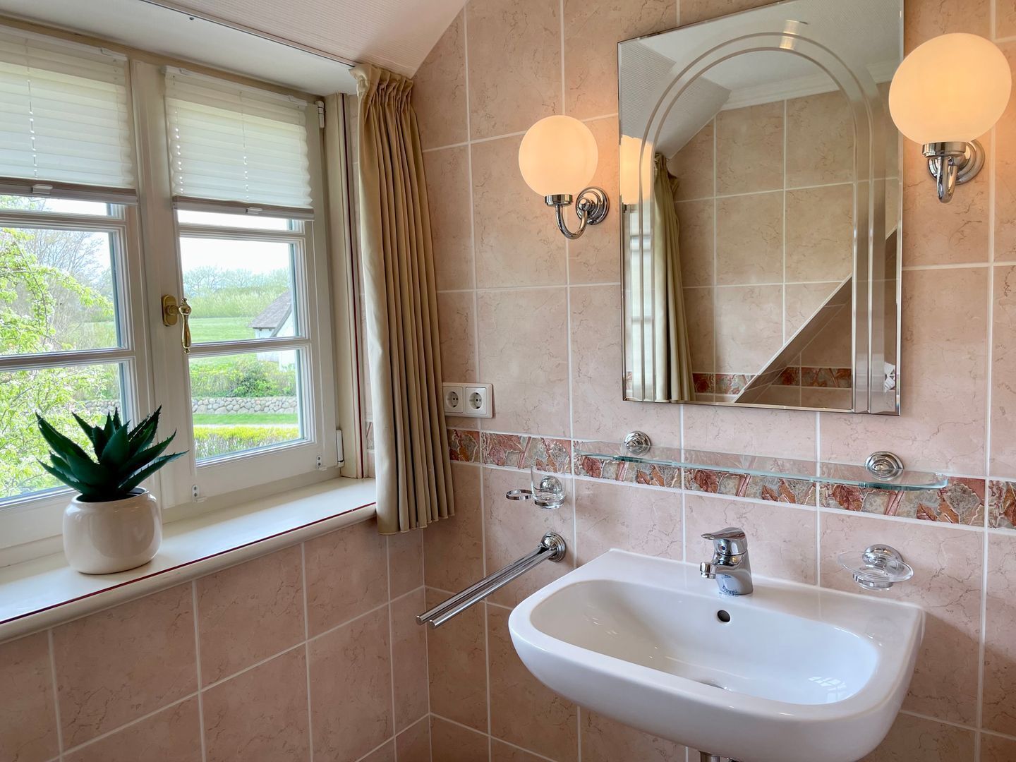 A bathroom with a window, a sink, a mirror, and a potted plant.