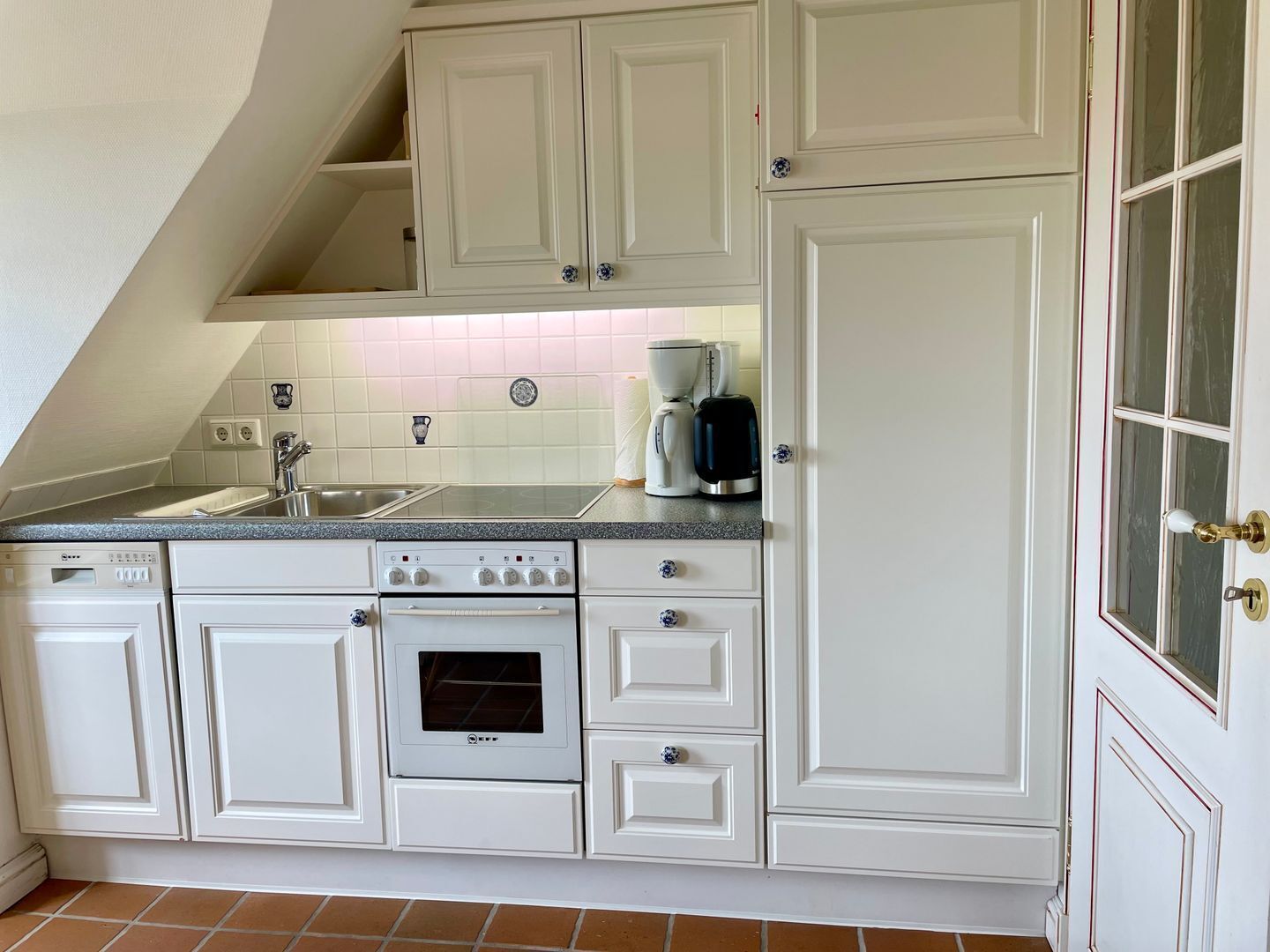 A kitchen with white cabinetry, a built-in oven, a coffee maker, and a sink.