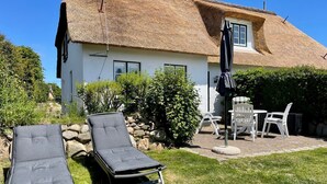 Une maison avec un toit de chaume, une terrasse avec des chaises longues et une petite table.