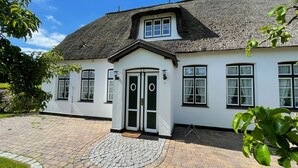 Une maison blanche avec un toit noir, une allée circulaire et un petit jardin.
