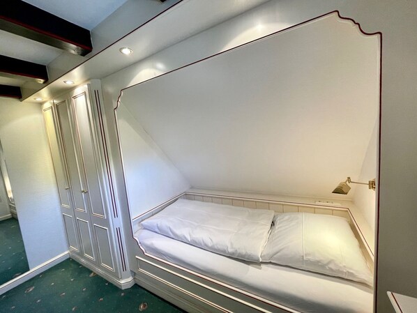 Habitación con cama individual, mesita de noche y lámpara fijada a la pared.