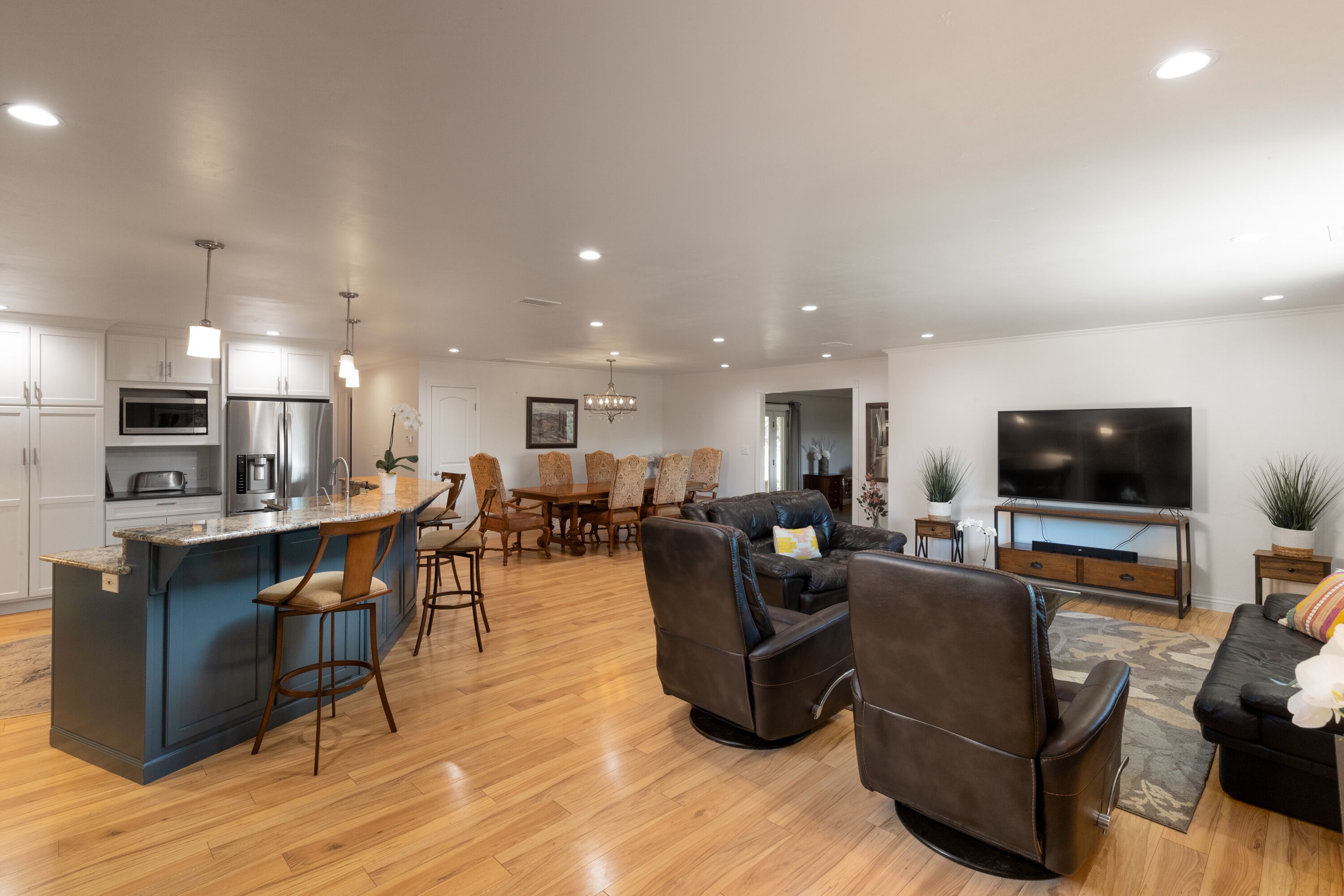 A modern kitchen with a bar area, a dining set, and a living room with a sofa and TV.