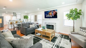 A modern living room with a fireplace, a flat-screen TV mounted on the wall, and a dining area in the background.