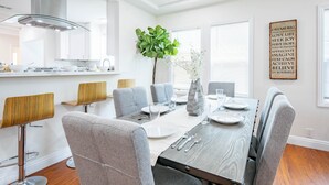 A modern dining area with a wooden table set for six, surrounded by grey upholstered chairs.