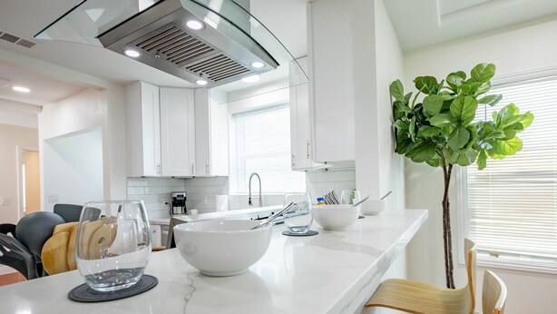 A modern kitchen with white cabinets, a marble countertop, and a central island with a bowl and glass.