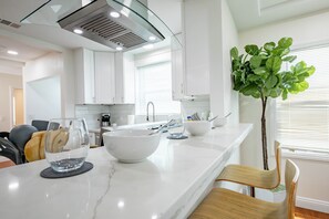 Uma cozinha moderna com armários brancos, bancada de mármore e uma ilha central com uma tigela e copos.