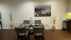 Ein Essbereich mit einem Glastisch, vier Stühlen, einem dekorativen Mittelstück und einem Stadtbild an der Wand.