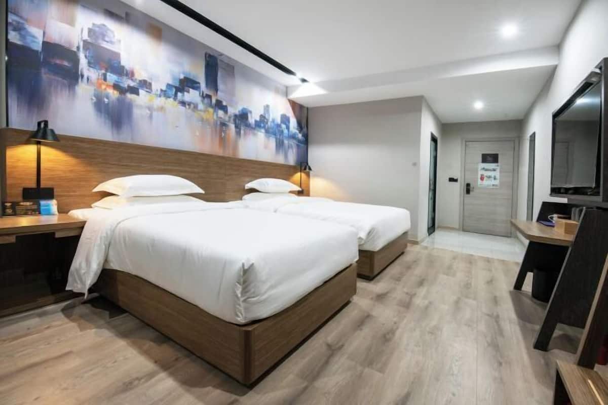 A modern hotel room with two beds, a large abstract cityscape painting, a desk with a lamp, and a mirror.