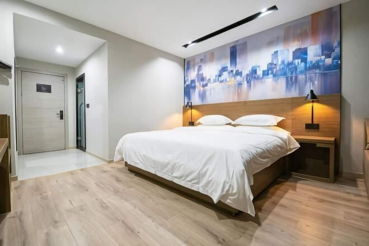 A modern hotel room with a large bed, wooden headboard, two bedside lamps, and a cityscape artwork on the wall.