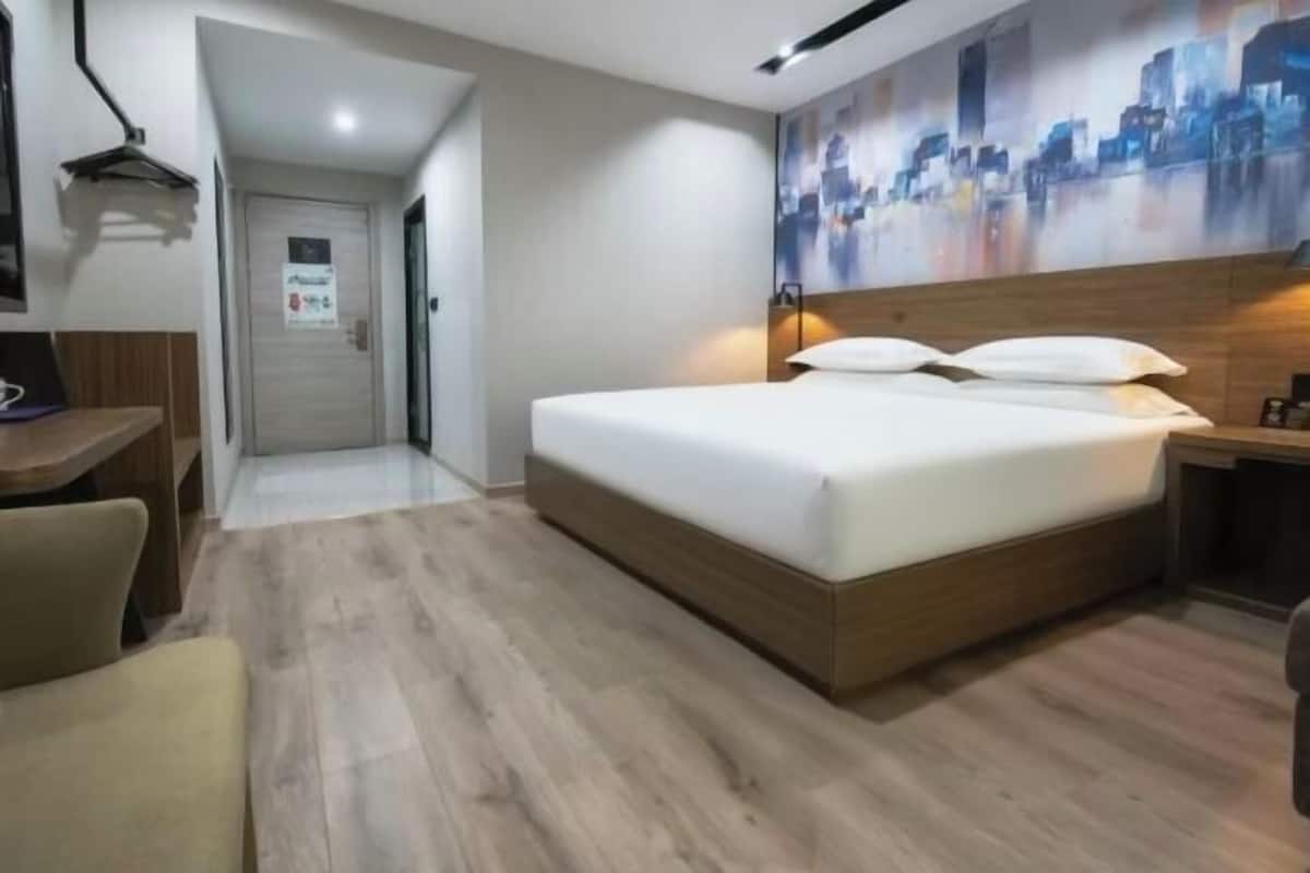 A modern hotel room with a wooden bed, a desk, and a cityscape mural on the wall.