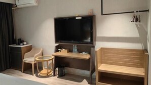 Une chambre d’hôtel équipée d’un téléviseur à écran plat, d’un bureau en bois, d’une chaise, d’une petite table ronde, d’un banc en bois et d’une poubelle.