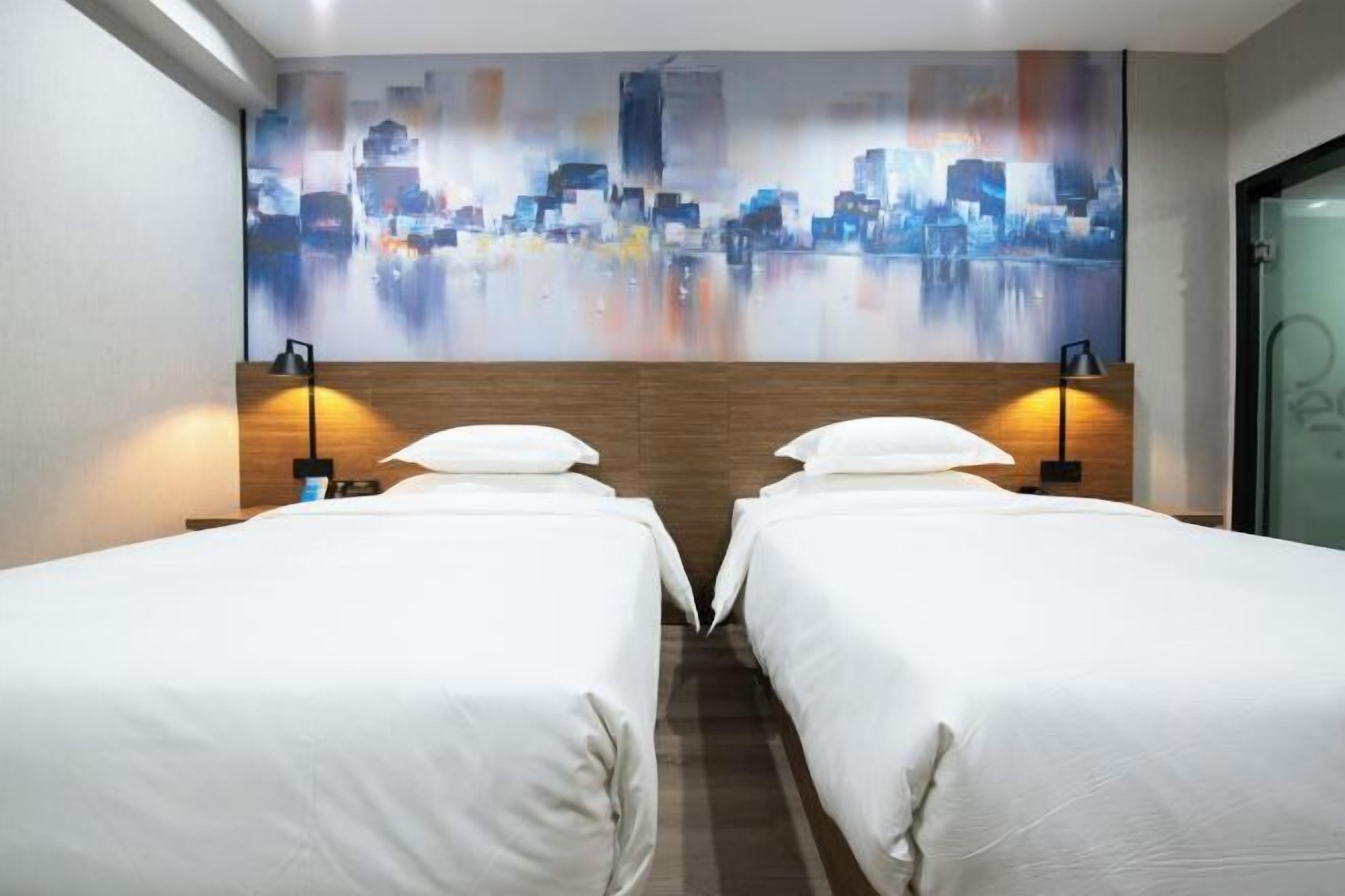 Ein Hotelzimmer mit zwei Betten, einem Stadtbild-Wandgemälde und einem hölzernen Kopfteil.