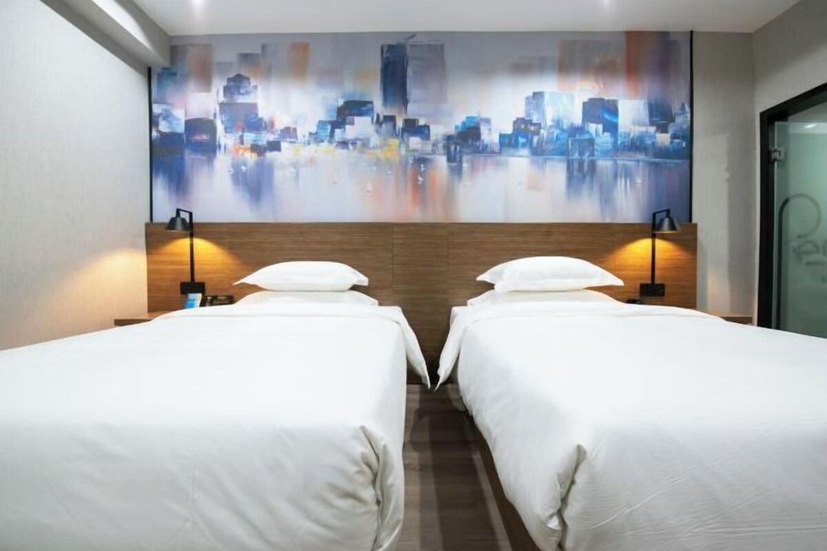 A hotel room with two beds, a cityscape mural, and a wooden headboard.