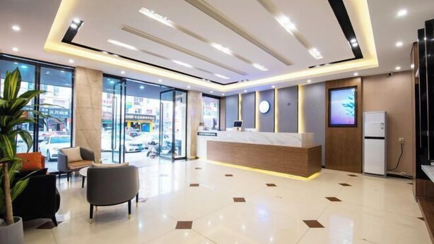A modern hotel lobby with a reception desk, seating area, and large windows offering a view of the street.