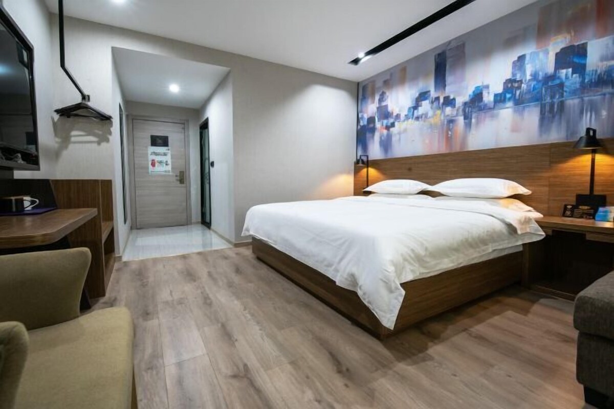 A modern hotel room with a wooden bed, a desk, and a cityscape mural on the wall.