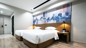 A modern hotel room with a large bed, two bedside tables, and a cityscape artwork on the wall.