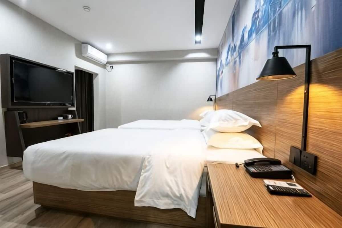 A hotel room with a bed, bedside table, lamp, and a TV.