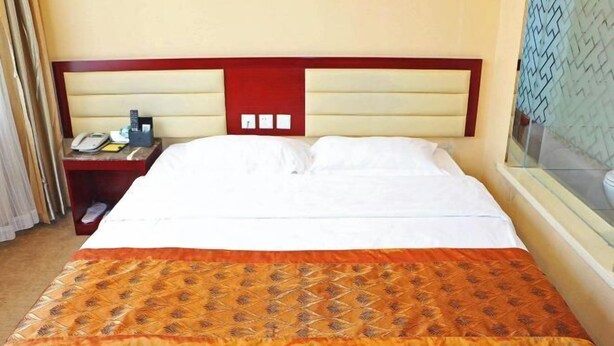 A hotel room with a bed, a nightstand with a phone and a lamp, and a window with a patterned view. - Jixi City Guesthouse (Jixi)