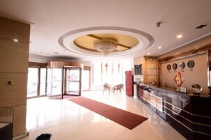 Un vestíbulo de hotel con una recepción, una alfombra roja y un candelabro.