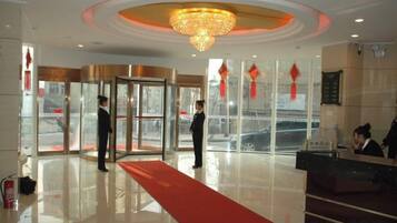 A hotel lobby with a reception desk, a red carpet, and a revolving door.