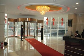 A hotel lobby with a reception desk, a red carpet, and a revolving door.