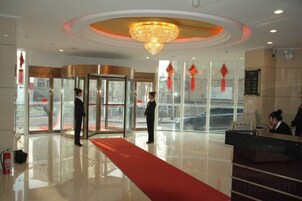 Un hall de hotel con una recepción, una alfombra roja y una puerta giratoria.