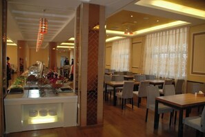 A hotel dining area with a buffet, multiple tables, and chairs.