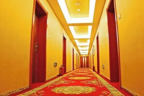 A hotel hallway with a red carpet, doors on both sides, and a ceiling with recessed lighting.