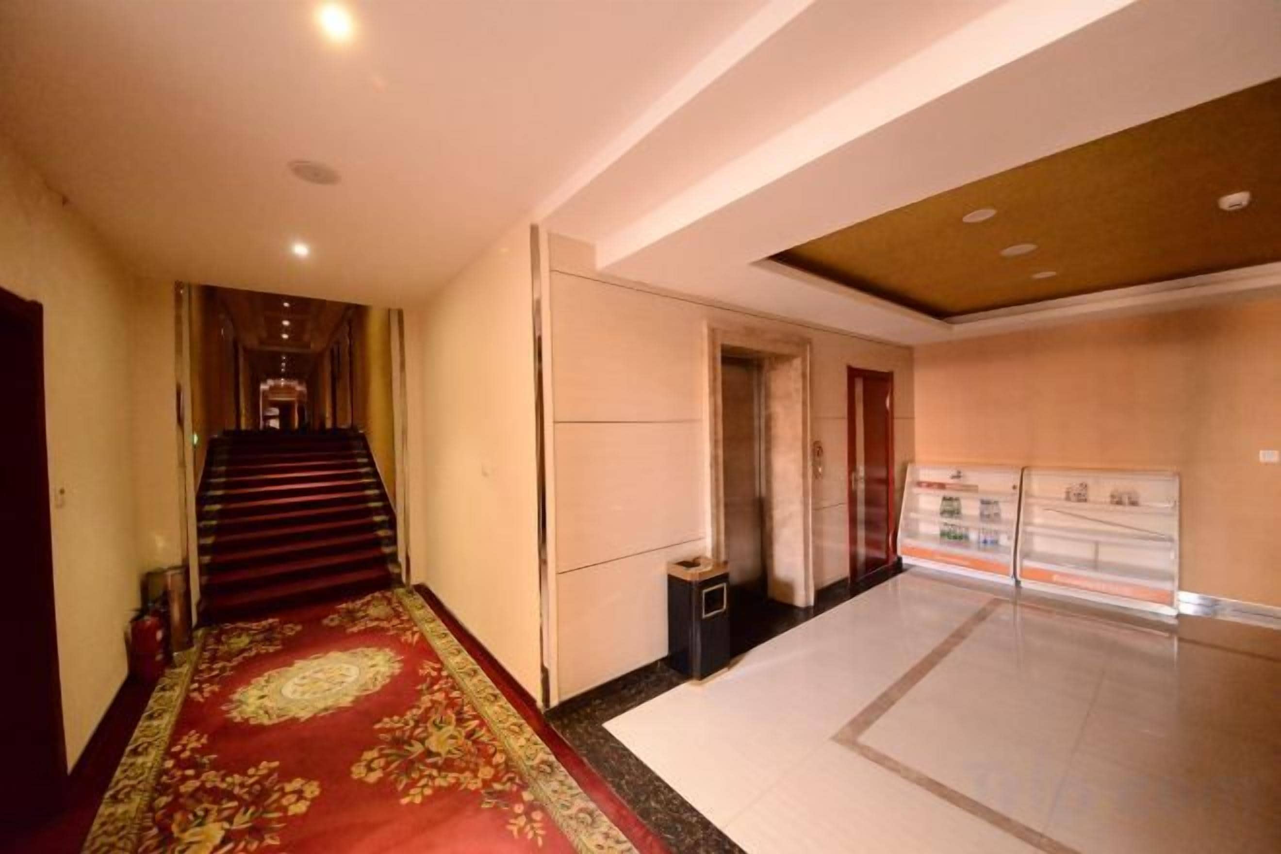 Corredor de hotel com escadas revestidas de carpete, um cesto de lixo e uma área de recepção.