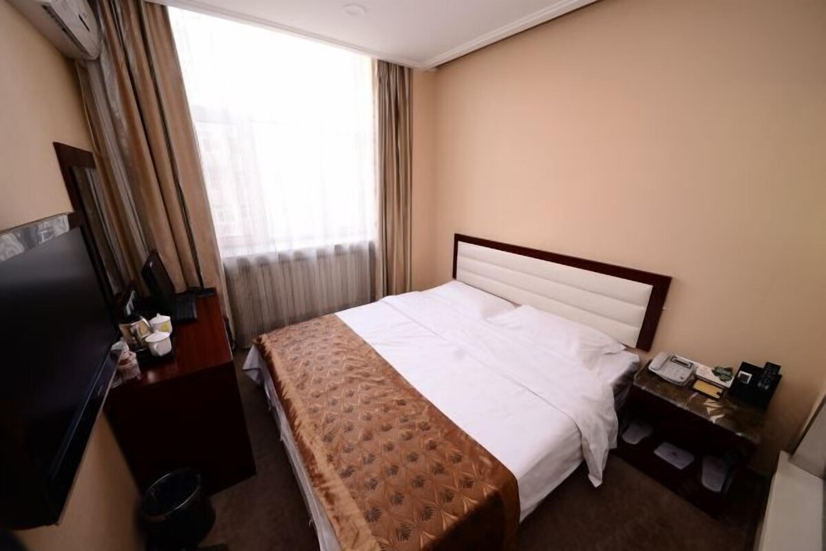 A hotel room with a bed, a desk with a telephone, a television, and a window with curtains.