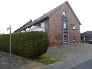 A two-story brick house with a blue ladder on the side, a hedge in front, and a street sign.