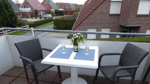 Un balcon avec deux fauteuils en osier et une table blanche, chacun agrémenté d’un set de table bleu et d’un verre de vin.