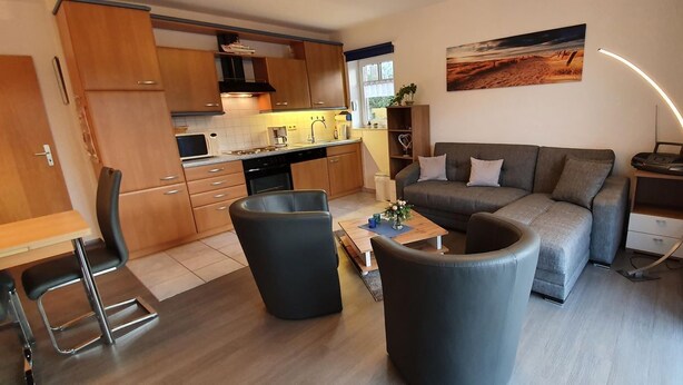 Une cuisine moderne avec des meubles en bois, un coin repas avec une table et des chaises, un canapé gris et un tableau accroché au mur.