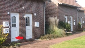 Un bâtiment en briques avec des portes numérotées, une porte blanche avec une fenêtre et une flèche rouge pointant vers cette porte.