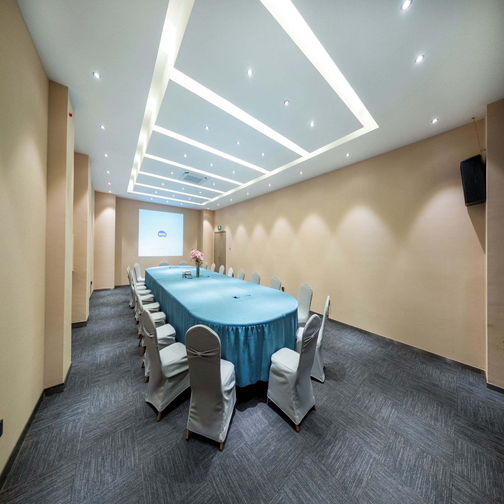 Una sala de conferencias con una larga mesa, sillas y una pantalla para proyector.