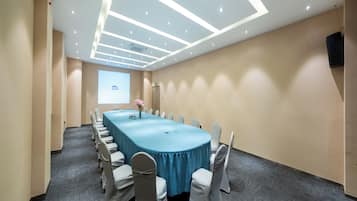 Una sala de conferencias con una larga mesa, sillas y una pantalla para proyector.