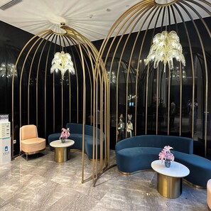 Eine moderne Lounge-Ecke mit einem blauen, gebogenen Sofa, einem pfirsichfarbenen Sessel und einem kleinen runden Tisch mit einer Blumenvase.
