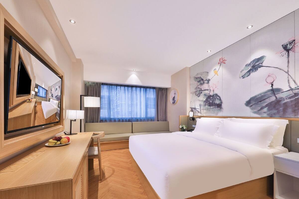 Una habitación de hotel moderna con una cama grande, un escritorio con una silla, un televisor y un ventanal con cortinas.
