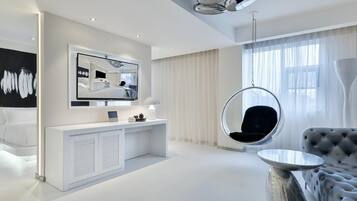 A modern hotel room with a large mirror, a hanging chair, a tufted sofa, and a round table.