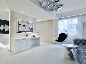 Una habitación de hotel moderna con un espejo grande, un sillón colgante, un sofá capitonado y una mesa redonda.