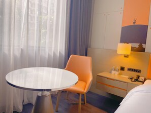 A hotel room with a round table, a single orange chair, a bed, a bedside table with a lamp, and a wall-mounted phone. - Crystal Orange Hotel Kunming Dongfenglu Henglong S (Kunming)