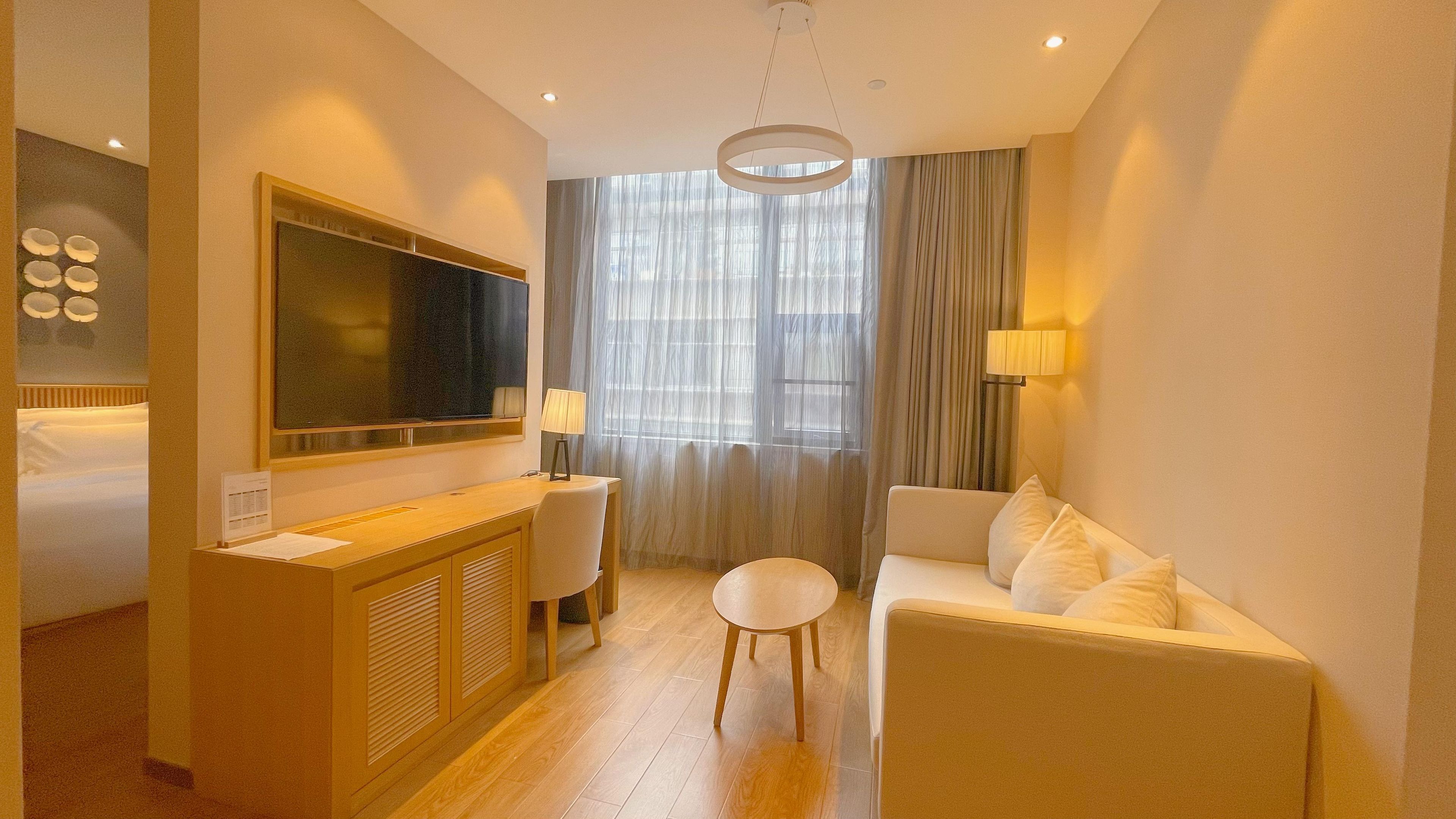 A hotel room with a bed, a desk, a TV, a sofa, and a window with curtains.