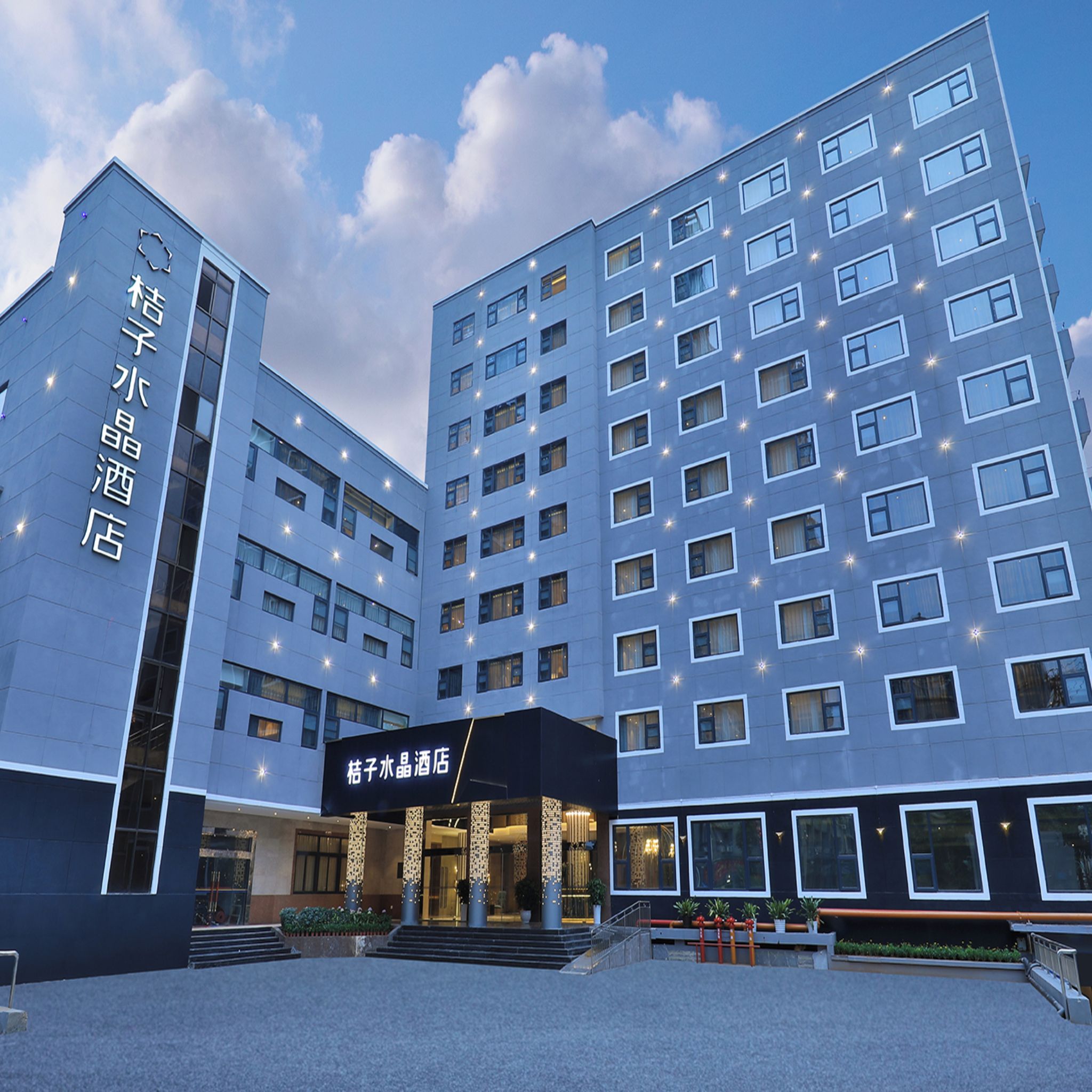 A modern hotel building with multiple floors, a prominent entrance with steps, and illuminated windows.